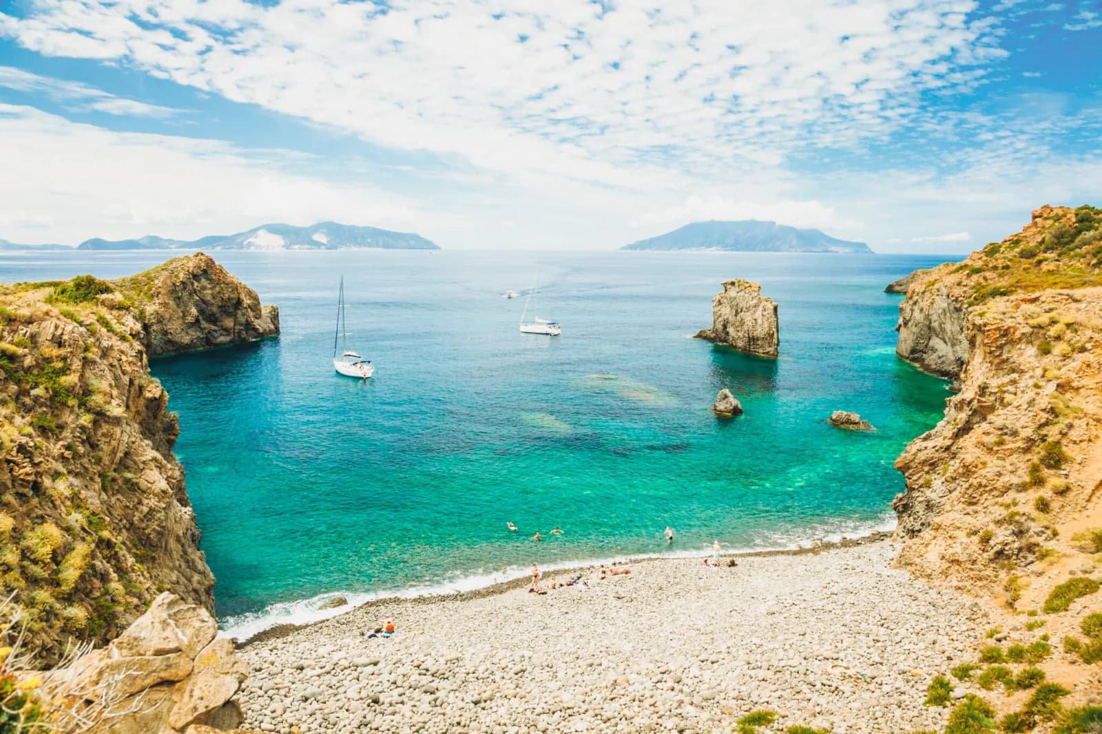 Cala Junco on Panarea — yachts anchored in a rocky turquoise cove, other Aeolian islands on the horizon